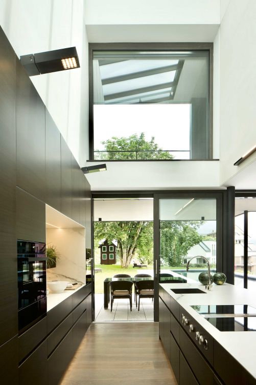 Grösse zeigt die Küche nicht nur in der Höhe, sondern auch in Richtung Garten. Die Schiebeverglasung ermöglicht einen schwellenlosen Übergang zur Terrasse mit Esstisch und zum Pool.