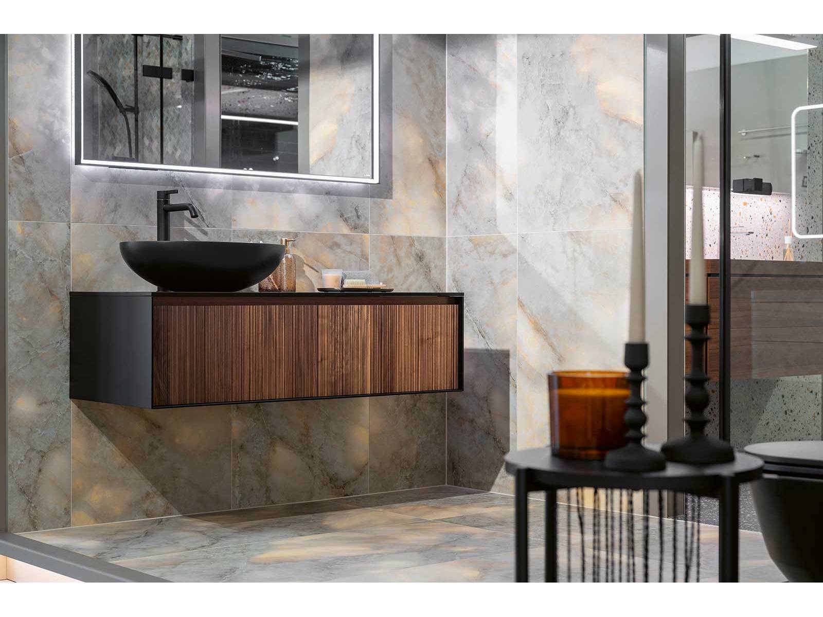 Feinsteinzeugplatten in matter und polierter Marmor-Bernstein-Optik treffen auf einen Unterbau in matt lackierter Holzstruktur und bringen Eleganz ins Bad. Der schwarze Aufsatzwaschtisch «Zante» und der passende Waschtischmischer «Bevo» setzen moderne Akzente. Das Unternehmen besitzt schweizweit fünf Ausstellungen für Bäder, Wand-, Bodenplatten und Parkett. HUG BAUSTOFFE.